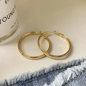 Elegante goldfarbene geometrische Kreolen mit polierter Metalloberfläche auf weißem Grund