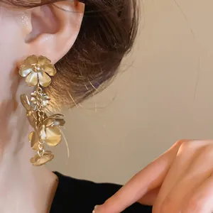 Détail rapproché de boucles d'oreilles pendantes à fleurs vintage en or mat sur un mannequin