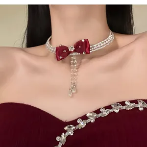 Close-up detail of a sparkling rhinestone choker featuring a red bow and pearl tassels