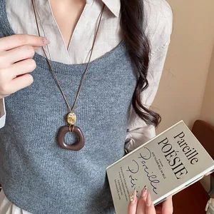 Dettaglio di una collana vintage con ciondolo in resina marrone su maglione grigio