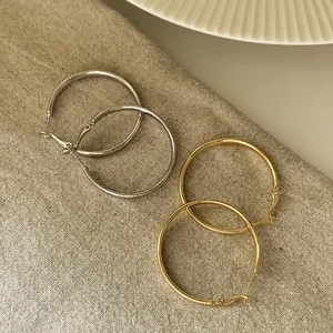 Detailansicht großer gold- und silberfarbener Metall-Creolen auf strukturiertem Leinen.