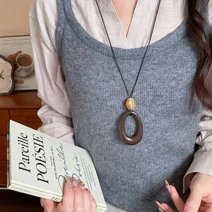 Vista dettagliata di una collana vintage con pendente ovale in resina su gilet grigio