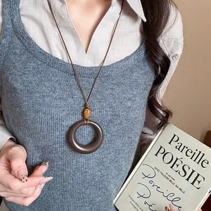 Primo piano di una collana etnica in resina con grande pendente circolare su un maglione grigio.