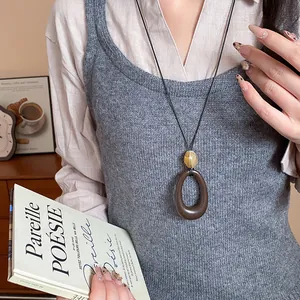 Vista dettagliata di una collana vintage con ciondolo ovale in resina su un gilet grigio