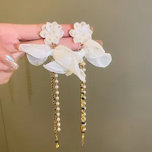 Close-up detail of white flower earrings with ribbon bows and long pearl tassels