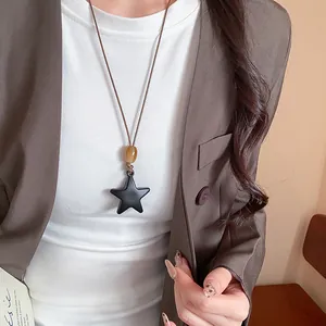 Primo piano di una collana vintage con ciondolo a stella in resina nera indossata su un blazer