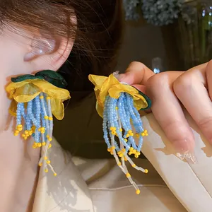 Close-up of handmade yellow flower earrings with long blue bead tassels on a model
