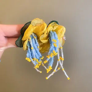 Close-up detail of handmade fabric flower earrings with light blue and yellow beaded tassels