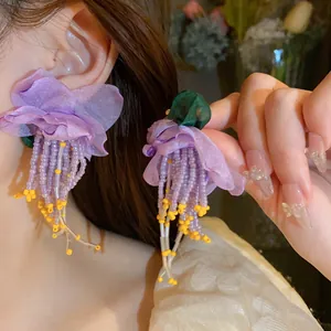 Macro view of purple fabric flower earrings with long beaded tassels on model's ear