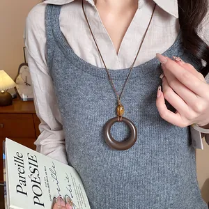 Dettaglio di una collana etnica vintage con ciondolo circolare scuro e perla occhio di tigre.