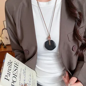Primo piano di una collana con ciondolo in resina nera stile etnico e blazer marrone.