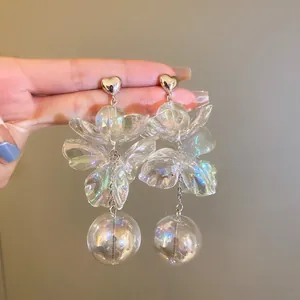 Close-up of iridescent flower earrings with transparent sphere tassels held by hand