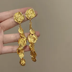 Dettaglio ravvicinato di orecchini pendenti dorati con una texture artistica in metallo martellato