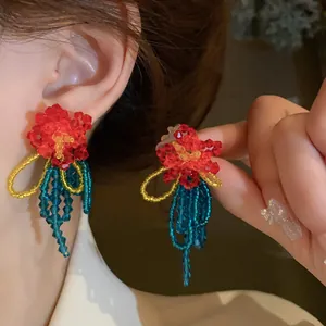 Detailed view of handmade red beaded flower earrings featuring elegant teal crystal tassels