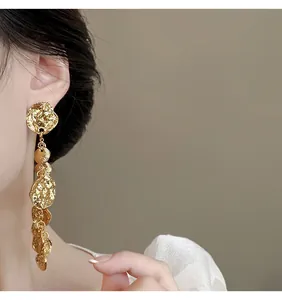 Primo piano dettagliato di orecchini a nappa in metallo martellato oro su una modella