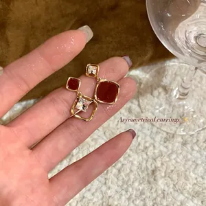 Close-up of elegant asymmetrical earrings with red stones and square zircons