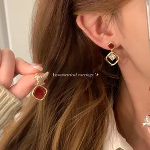 Close-up of vintage asymmetrical earrings with red stone and zircon on ear and hand