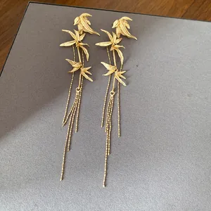 Elegant gold bamboo leaf dangle earrings with long beaded tassels on grey background