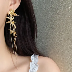 Detailed close-up of elegant gold bamboo leaf tassel earrings on an Asian model