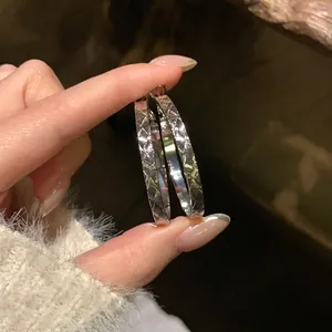 Dettaglio ravvicinato di orecchini a cerchio in argento con trama incrociata elegante