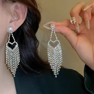 Dettaglio di lunghi orecchini a nappa con design a cuore in zircone su modella.
