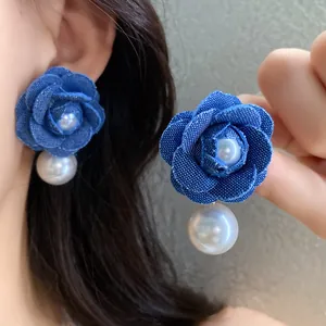 Primo piano dettagliato di orecchini a fiore in denim blu con pendenti di perle per donne.