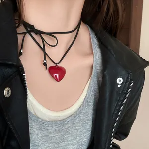 Detail view of a glossy red heart resin necklace with adjustable black cord on model.