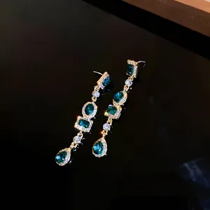 Primer plano de pendientes largos con cristales verdes geométricos y pedrería brillante