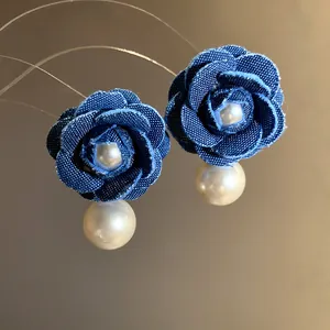 Dettaglio macro di orecchini a rosa in denim blu con eleganti accenti di perle pendenti.