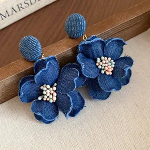 Primo piano di orecchini a fiore in tessuto denim blu con pistilli in colori pastello.