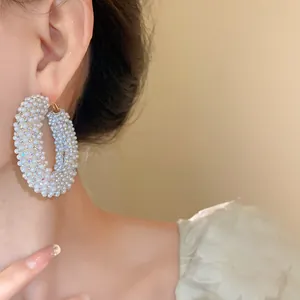 Detailaufnahme von großen Boho-Creolen mit weißen Perlen und glitzernden Strasssteinen