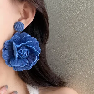 Primo piano di orecchini a fiore in tessuto denim blu indossati da una modella