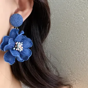 Vista dettagliata di un orecchino a fiore in denim blu fatto a mano indossato sull'orecchio