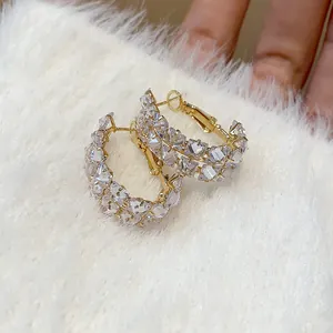 Detailed macro view of double-row zircon oval hoop earrings on white fur background texture