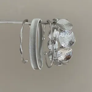 Close-up of textured silver metal bracelet set hanging on a minimalist display rod