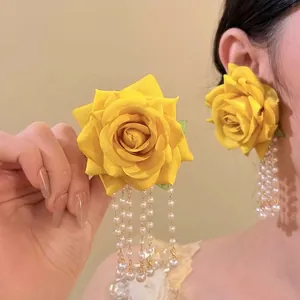 Detailansicht gelber Raffia-Rosenohrringe mit eleganten Perlenquasten an einer Frau