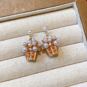 Detail of gold-plated stud earrings with elegant pearls and vibrant orange zircon stones.