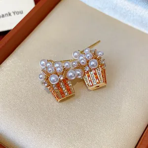 Macro detail of cute popcorn-shaped earrings with pearls and orange zircons.