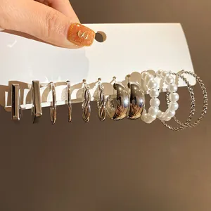 Close-up of a silver-toned earring set featuring pearl and twisted hoop designs on a white card