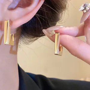 Close-up of elegant gold geometric stud earrings worn on ear and held by hand