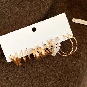 Detail shot of a vintage gold earring set with pearls and twisted hoops on a textured background.