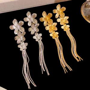 Λεπτομέρεια από ασημένια και χρυσά σκουλαρίκια λουλούδια με μακριές φούντες από στρας.