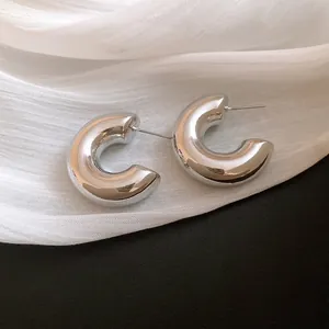 Detailed macro view of chunky silver C-shaped hoop earrings on white draped fabric