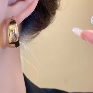 Close-up of elegant gold wide hoop earring worn by a model in soft warm lighting