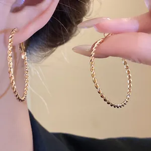 Macro shot of large gold-tone twisted rope hoop earrings showing intricate texture