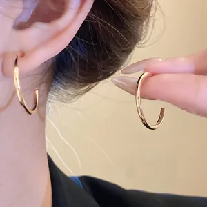 Detailed macro view of polished gold minimalist hoop earrings shown on ear and being held