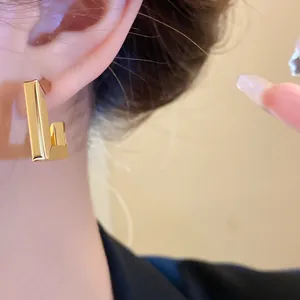 Close-up detail of a minimalist gold geometric L-shaped stud earring worn on the ear