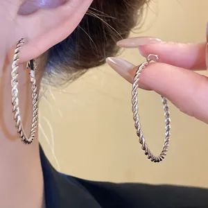 Detailed view of vintage style twisted rope silver hoop earrings on ear and hand