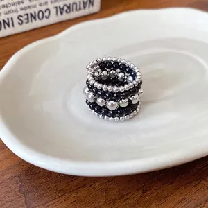 Anillo retro multicapa con cuentas plateadas y negras sobre un plato de cerámica