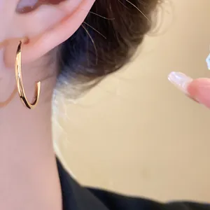Close-up detail of a minimalist gold-plated C-shaped hoop earring on ear